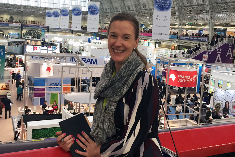 Briana leaning on red balcony overlooking the London Book Fair