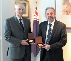 Two men holding medals in front of Australian flag