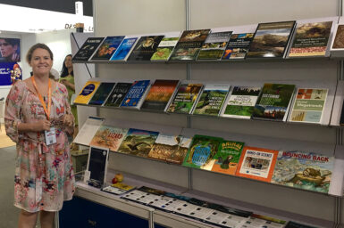 Smiling woman standing next to large wall display of books and brochures