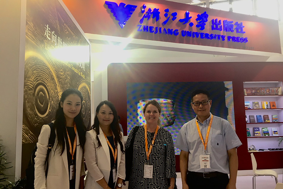 Three women and a man smiling in front of the Zhejiang University Press exhibition booth