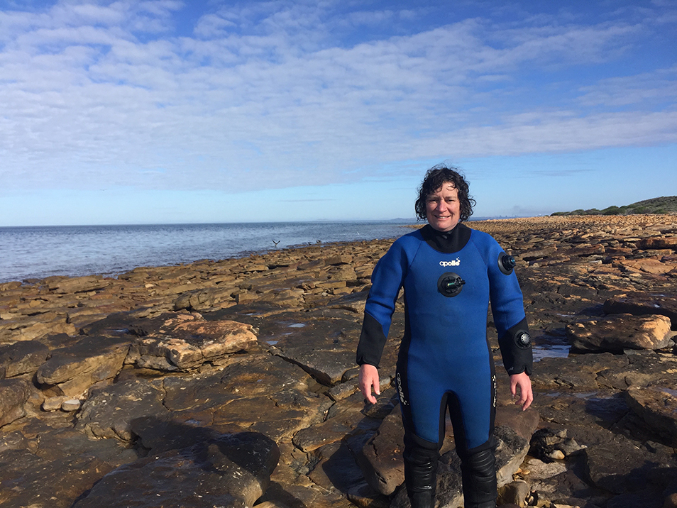 Person in wetsuit standing outside on rocks