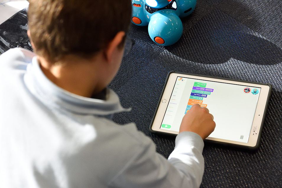 A child with short brown hair using an iPad app to code.
