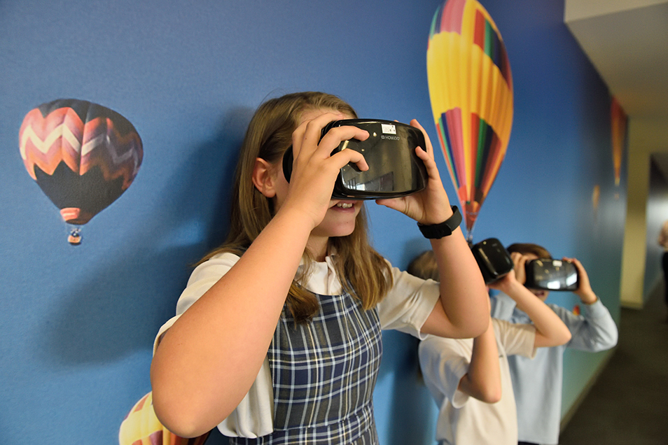 Girl in school uniform holding a VR headset to her face.