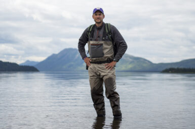 Dr Aaron Wirsing standing in water in front of mountains in Bristol Bay, Alaska.