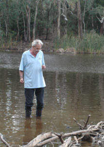 Michael Tyler in gumboots standing in the shallows of a bushland lake