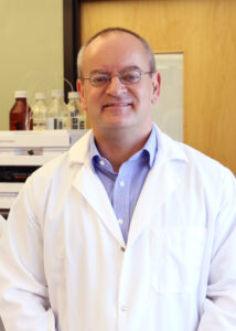 Professor Jamie Lead standing in a lap wearing a white lab coat