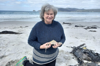 Author Anne Morgan kneeling on a Tasmanian beach holding the dried body of a weedy seadragon.