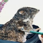 A close up photo of a person's hand holding a thin paintbrush over an illustration of a Gilbert's Potoroo emerging from a cloth bag.