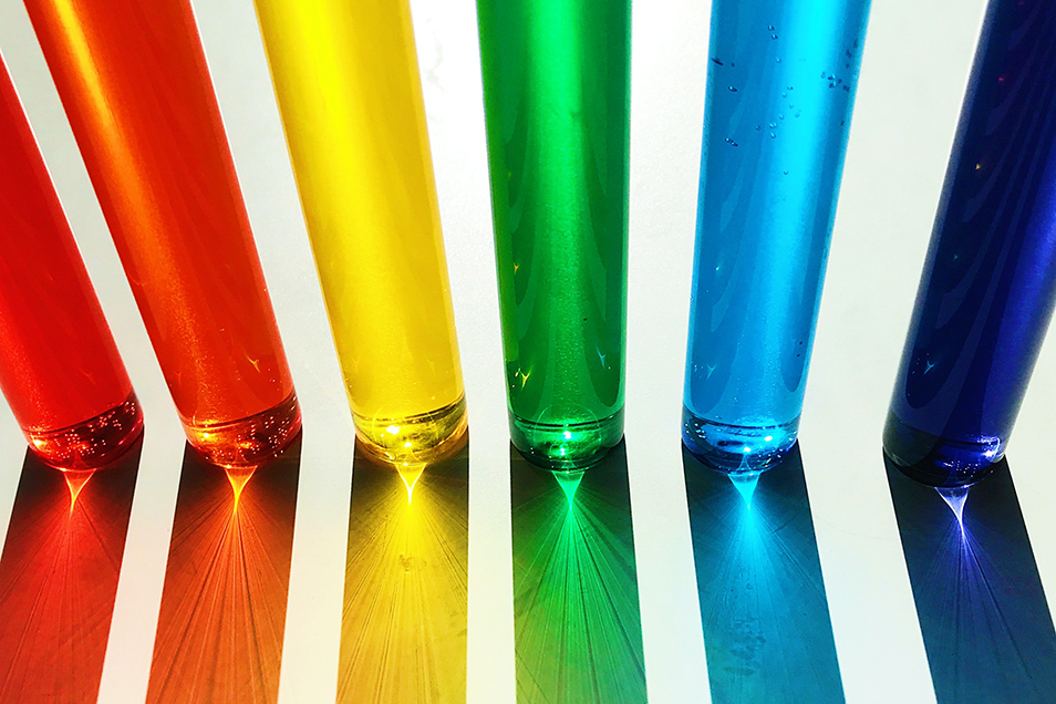 A row of glasses filled with coloured water, arranged in the colours of the rainbow.