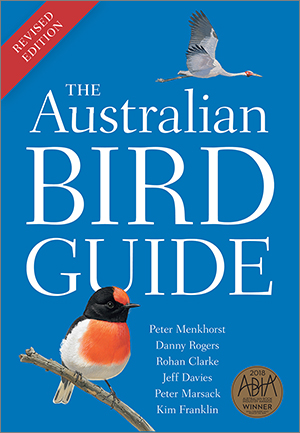 Cover of 'The Australian Bird Guide' featuring a brolga flying over the white title with a red-capped robin in the foreground perched on a branch. The cover is blue with a red 'Revised Edition' ribbon on the top left corner.