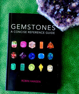 A copy of Gemstones: A Concise Reference Guide against a green spotted background and a piece of amethyst in the top right corner