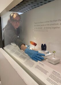 Author Robin Hansen leaning into a glassed cabinet case installing a gemstone called Tanzanite