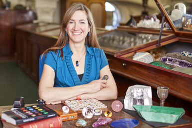 Author Robin Hansen sitting at desk and smiling surrounded by books and gemstone specimens