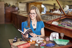Author Robin Hansen sitting at desk and reading her book surrounded by gemstone specimens