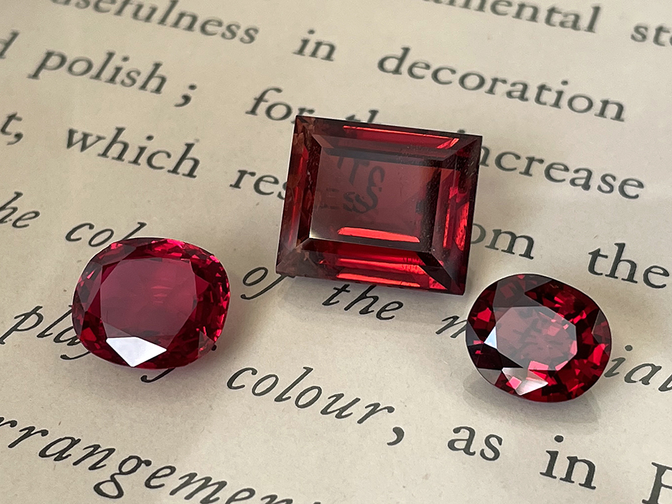 Three red spinel gemstones, two rounded and one square cut, sitting on a page of writing