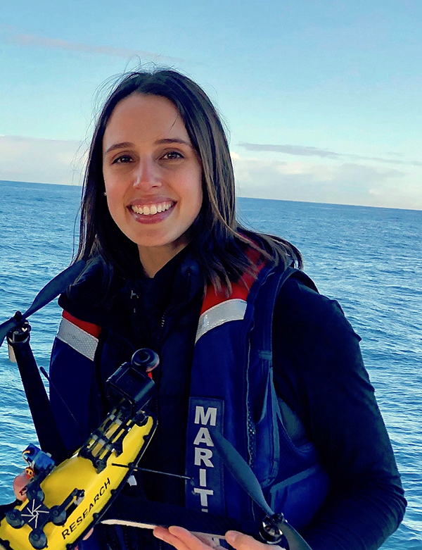 Vanessa Pirotta out at sea, wearing a buoyancy vest and holding a bright yellow research drone.