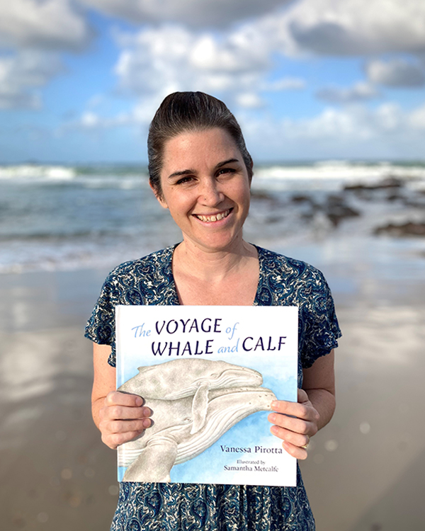 Samantha Metcalfe holding a copy of 'The Voyage of Whale and Calf' at a beach.