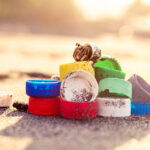 A pile of bottlecaps on the beach with a hermit crab using one as a home.