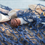 Plastic debris including a water bottle and straws, tangled in a fishing net and washed up on a beach.