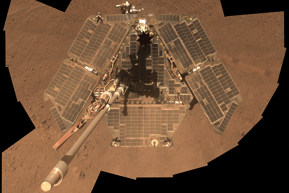 Multiple small photos stitched together to create a 'selfie' of a rover on Mars, looking down at its dusty solar panels.
