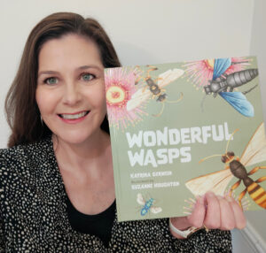Katrina Germein smiling and holding up the picture book 'Wonderful Wasps'.