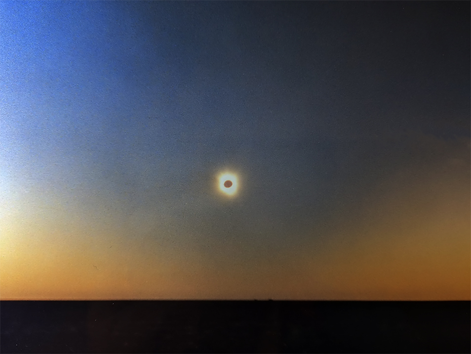 A total eclipse in the centre of the photo surrounded by a sky that shade from deep blue to a golden yellow.