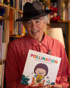 Christopher Cheng wearing a red shirt and a fedora, holding a copy of his book 'Pollination'.