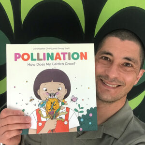 Danny Snell smiling to the camera against a green and black background and holding a copy of his book 'Pollination'.