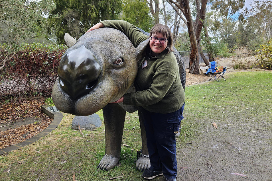 Bronwyn Saunders hugging a life-size diprotodon sculpture, smiling at the camera.